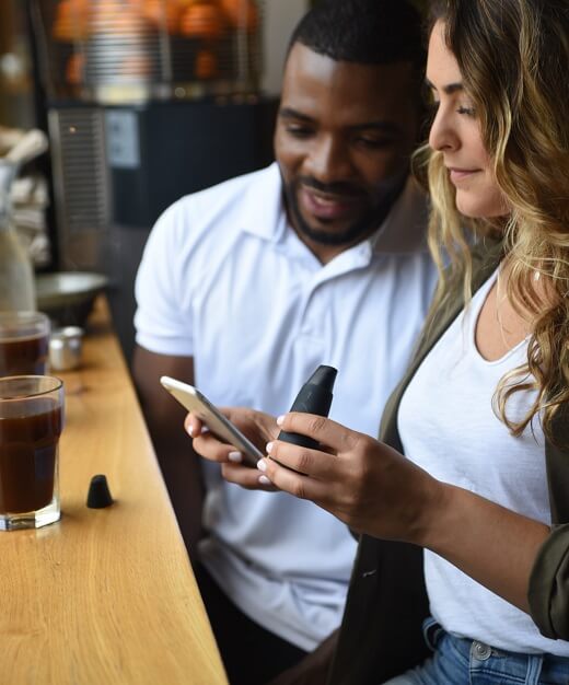 Two people are looking at a cell phone and the device