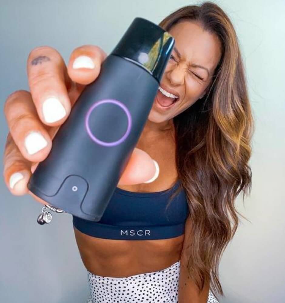 A woman in sportswear winks holding a Lumen device